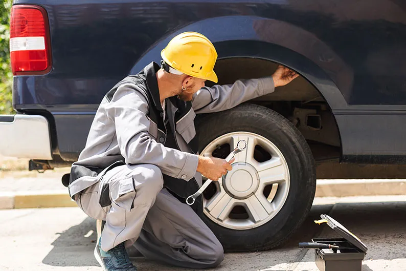 A worker in a hard hat fixing a flat tire outdoors.